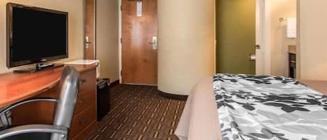 A hotel room with a bed, a desk with a chair, a television, and a carpeted floor.