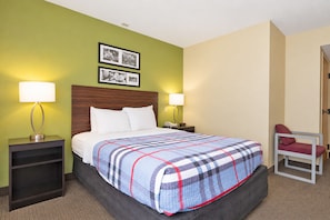 Quarto de hotel com uma cama, duas mesas de cabeceira, uma cadeira e um painel com quadros.