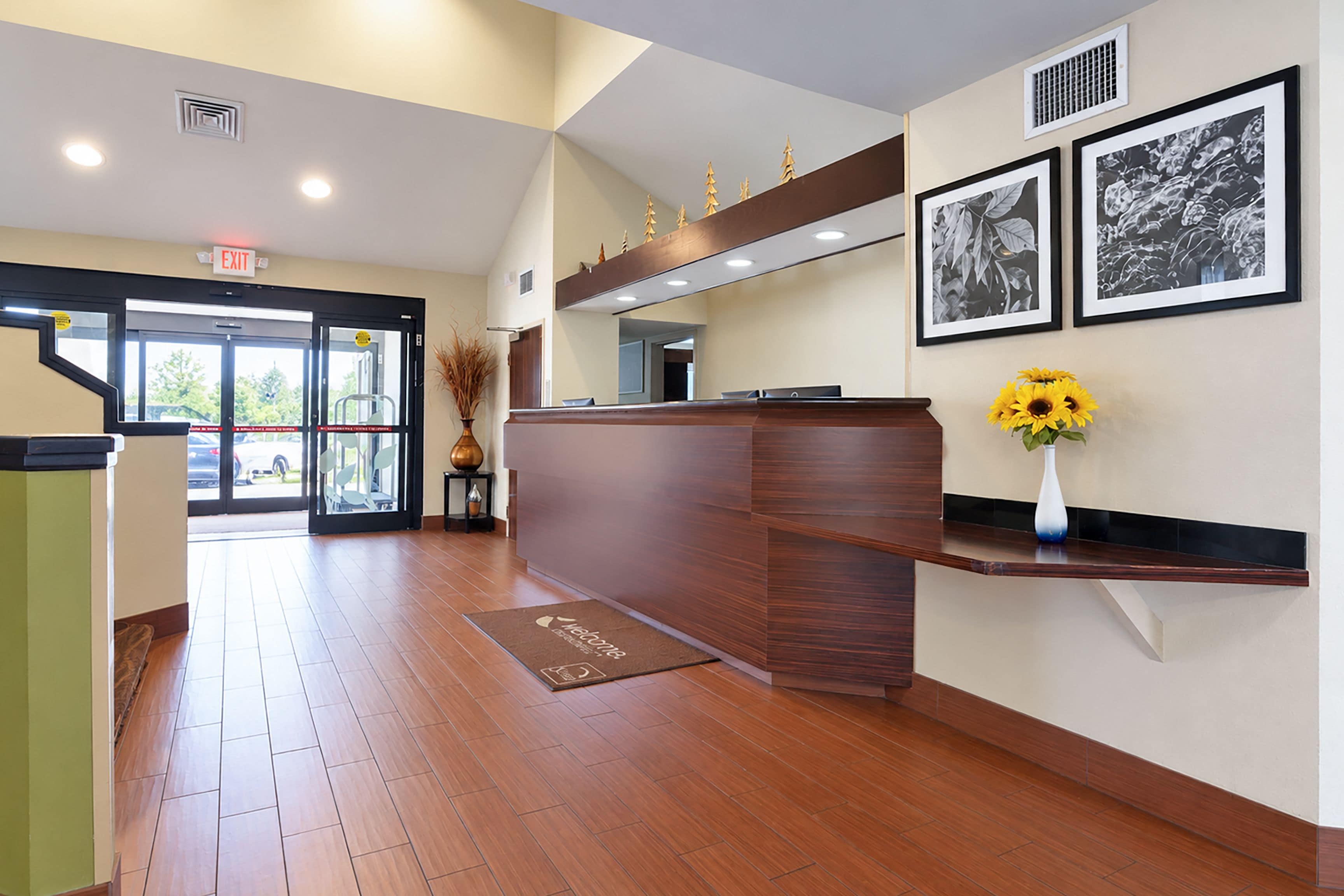 A reception area with a wooden reception desk, a doormat, a vase with sunflowers, and framed black and white photographs on the wall.