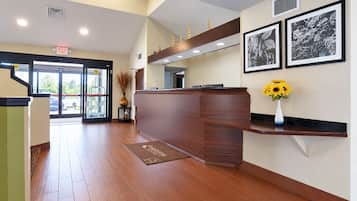 A reception area with a wooden reception desk, a doormat, a vase with sunflowers, and framed black and white photographs on the wall.