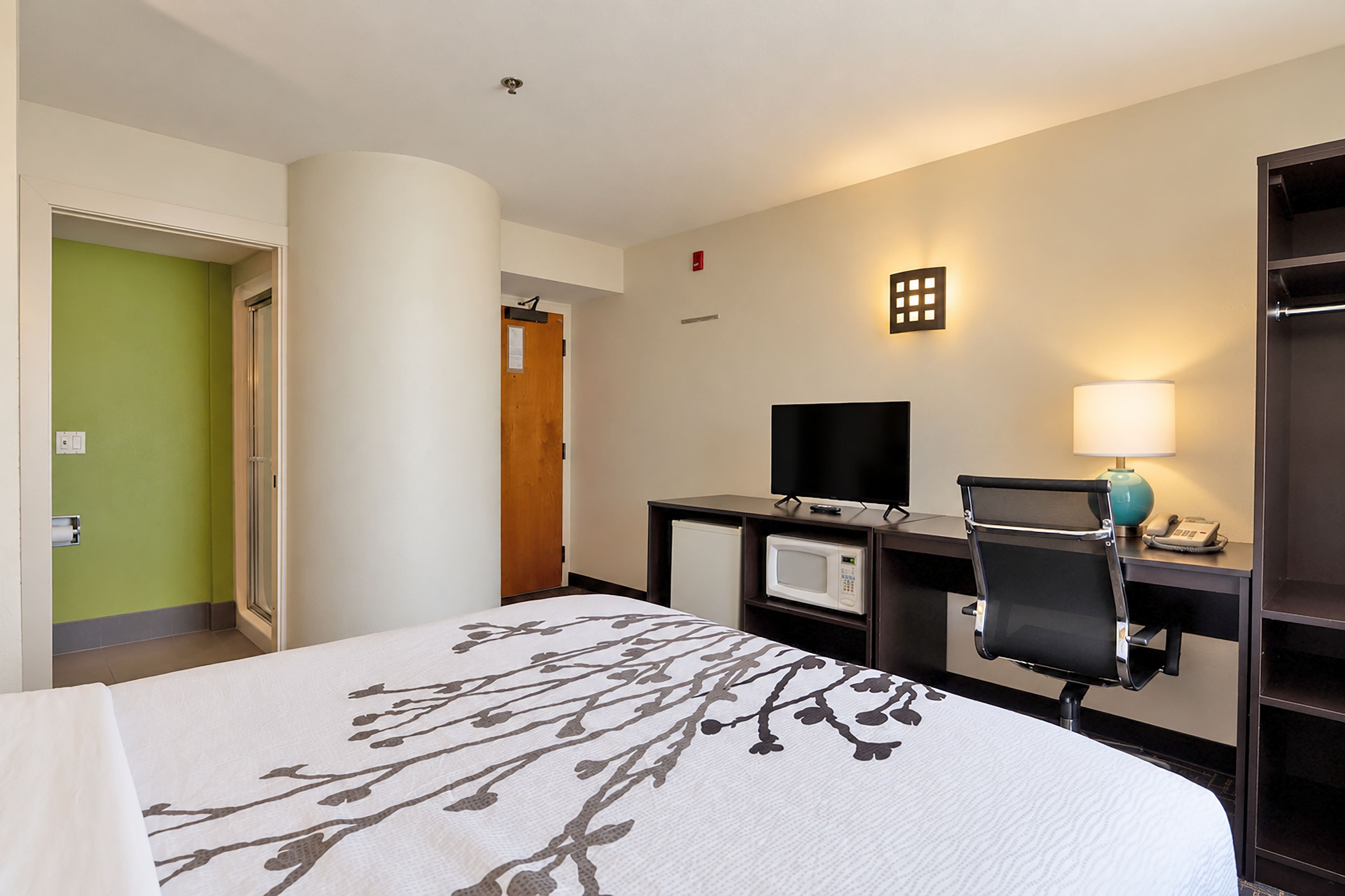 A hotel room with a bed, a desk with a computer, a microwave, and a TV.