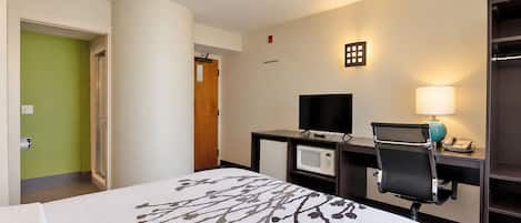 Una habitación de hotel con cama, escritorio con computadora, microondas y televisión.