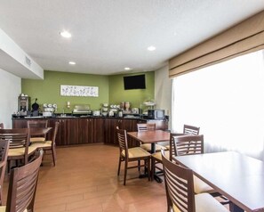 A dining area with wooden tables and chairs, a kitchen area with appliances, and a television mounted on the wall. - The Douillet by Demeure Hotels (Oklahoma City)
