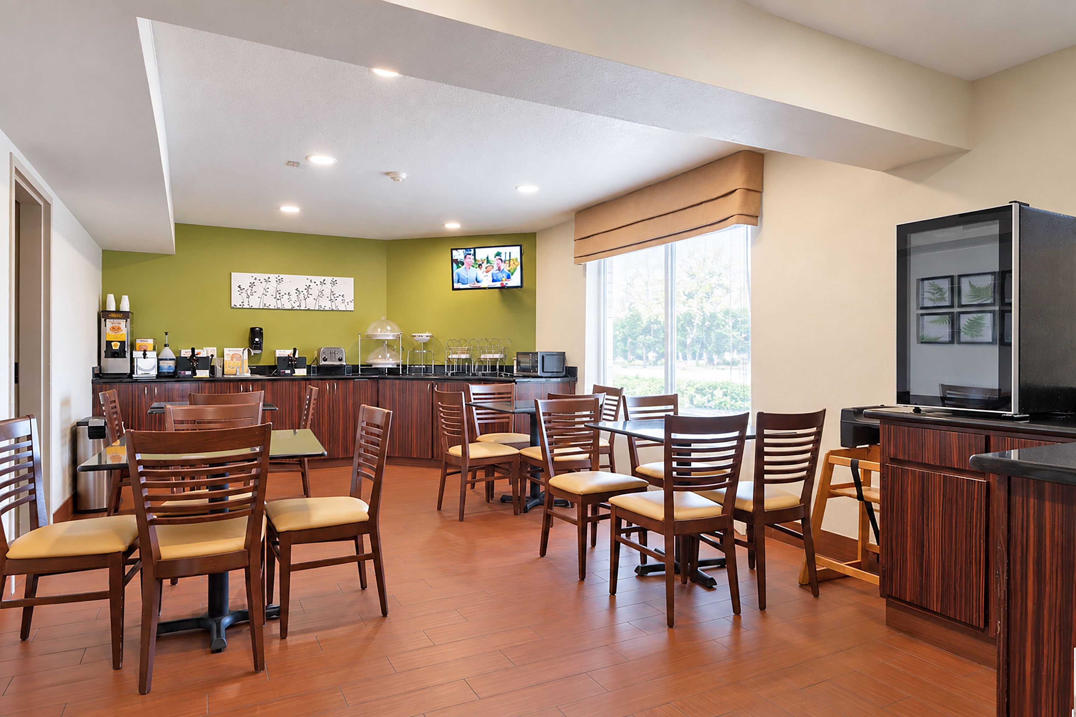 A restaurant with wooden chairs and tables, a bar area, and a television screen.