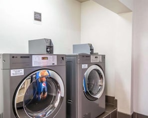 A laundry facility with two commercial washers and dryers, a sign indicating rental availability, and a wall-mounted control panel. - The Douillet by Demeure Hotels (Oklahoma City)