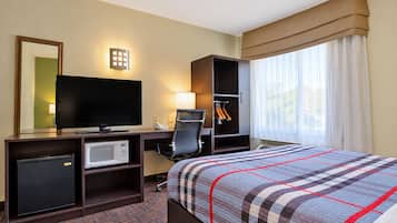 A hotel room with a bed, a desk with a television, a microwave, and a wardrobe.