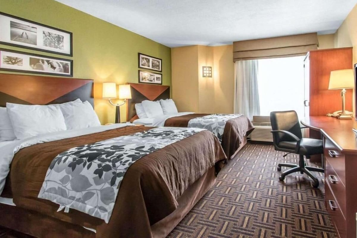 Habitación de hotel con dos camas, un escritorio, una silla y una ventana con cortinas.