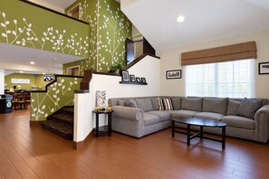 A modern living room with a grey sectional sofa, a coffee table, and a staircase with green walls and white leaf patterns.
