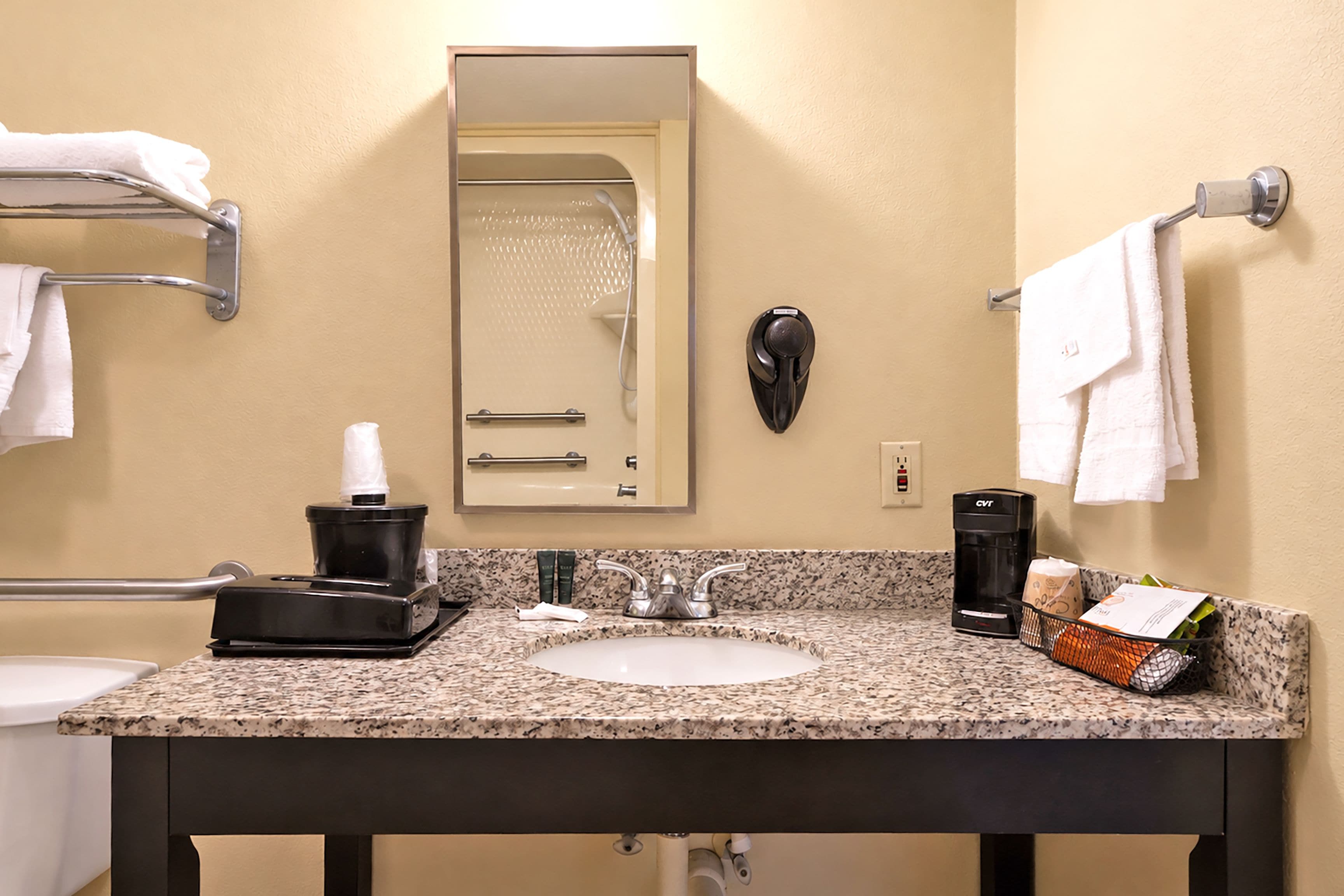 A bathroom with a sink, mirror, towel rack, and a coffee maker.