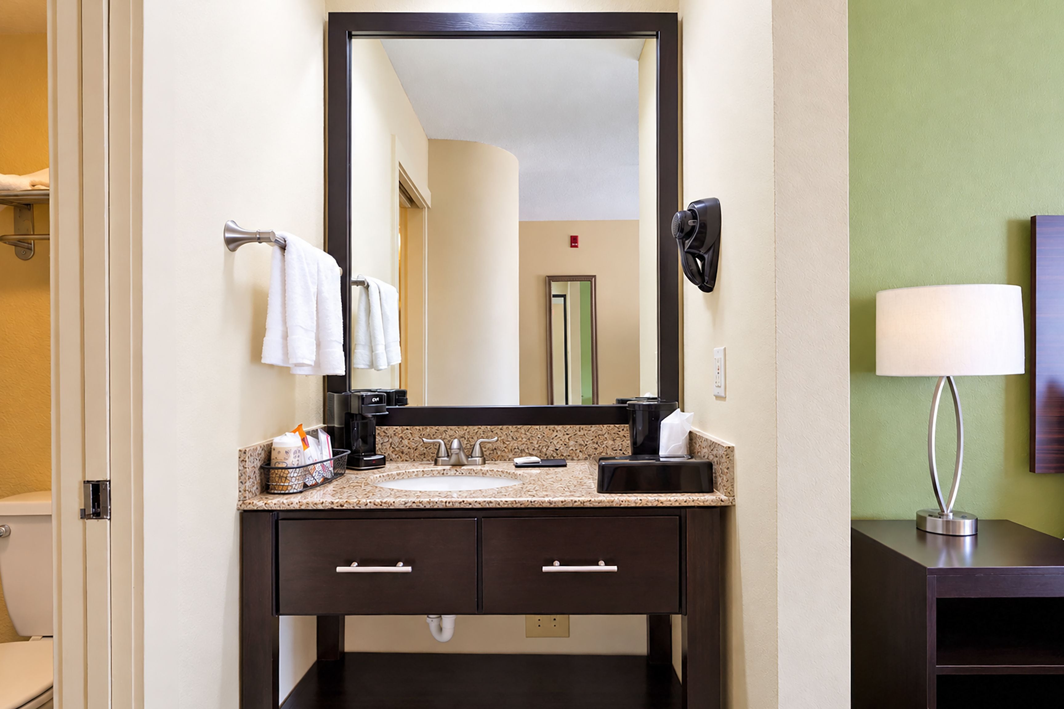 Une salle de bain d’hôtel avec un meuble-lavabo en bois foncé, un évier et un grand miroir.