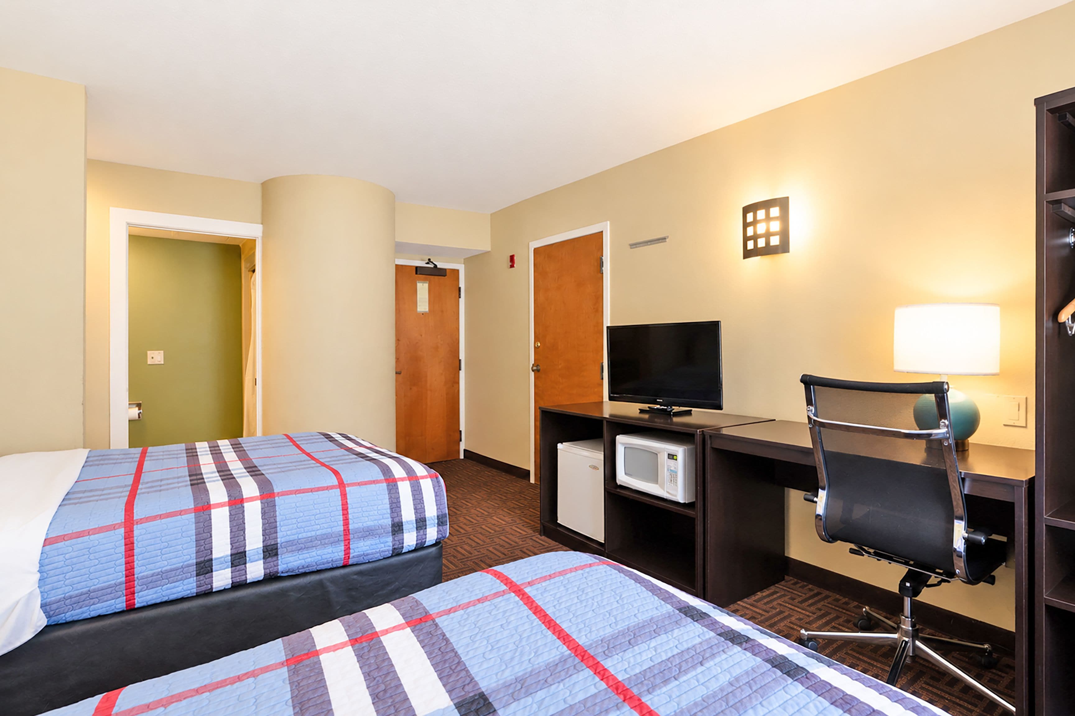 Una habitación de hotel con dos camas, un escritorio con computadora, televisor y una silla.
