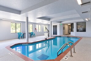 An indoor swimming pool with clear water, surrounded by white walls and a tiled floor.