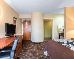 Een hotelkamer met een bed, een bureau met een televisie, een stoel, een grote zuil en een deur naar een andere kamer.