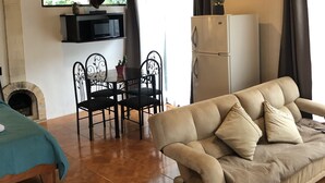 Una sala de estar acogedora con un sofá, una chimenea, un comedor con sillas, un televisor montado en la pared y un refrigerador.