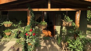 Una casa de madera con porche cubierto, plantas en macetas y un pequeño jardín.