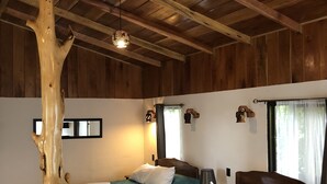 Una habitación con vigas de madera, dos camas con ropa de cama azul turquesa, un tronco de árbol de madera y una lámpara colgante.