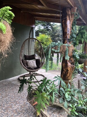 A wicker chair with cushions, a hanging plant, and a tree trunk in a covered outdoor area. - welcoming you into our home with a luxurious private space of your own! (Monteverde)