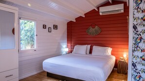 Slaapkamer met een groot bed, witte muren, een rode accentmuur, houten vloeren, een raam en een wandairconditioner.