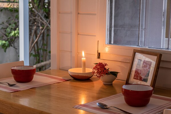 A dining table with red bowls, a candle, and a framed picture.