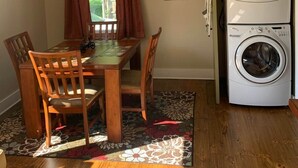 A dining area with a table and chairs, a window with curtains, and a stacked washer and dryer unit. - The Edinburgh Cottage (Baton Rouge)