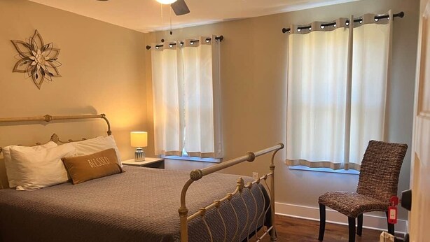 A bedroom with a bed, a chair, a ceiling fan, and curtains. - The Edinburgh Cottage (Baton Rouge)