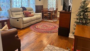 A living room with a sofa, a coffee table, a dining table with chairs, a TV, and a Christmas tree. - The Edinburgh Cottage (Baton Rouge)