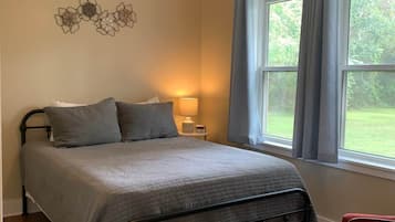 Ein Schlafzimmer mit Bett, Deckenventilator, Nachttisch mit Lampe und einem Fenster mit Vorhängen.