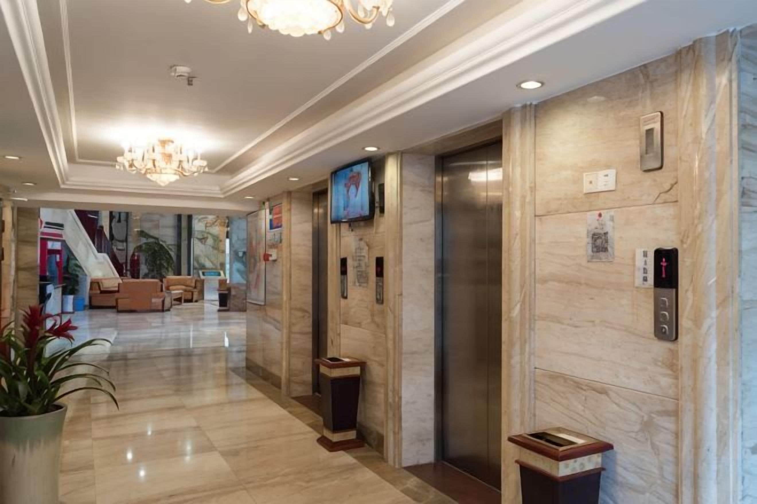 A hotel lobby with a marble floor, a reception desk, an elevator, and a television screen.