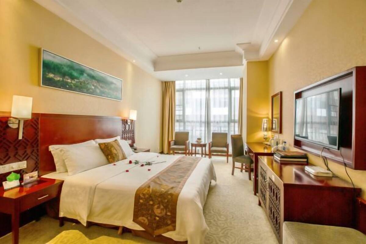 Une chambre d’hôtel avec un grand lit, un bureau avec une télévision, une chaise et une fenêtre avec des rideaux.
