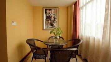 Un comedor con una mesa redonda y cuatro sillas de mimbre, un jarrón con una planta y un cuadro en la pared.