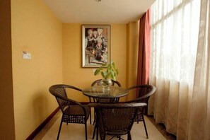 Un comedor con una mesa redonda y cuatro sillas de mimbre, un jarrón con una planta y un cuadro en la pared.