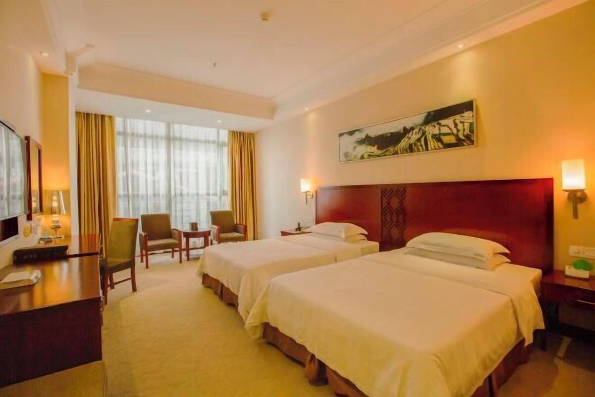 Une chambre d’hôtel avec deux lits, un bureau, une chaise, une télévision et un tableau au mur.