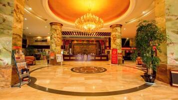 A hotel lobby with a grand chandelier, marble columns, and a reception desk.