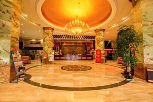 A hotel lobby with a grand chandelier, marble columns, and a reception desk.