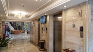 A hotel lobby with marble flooring, a chandelier, an elevator, and a television on the wall. - Golden Lusheng International Hotel (Rongshui)