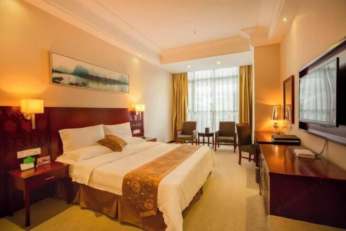 Une chambre d’hôtel avec un grand lit, un bureau, une télévision et un tableau au mur.