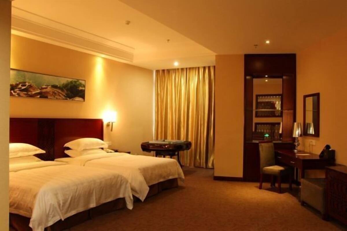Une chambre d’hôtel avec deux lits, un bureau, une chaise, une bibliothèque et un tableau au mur.