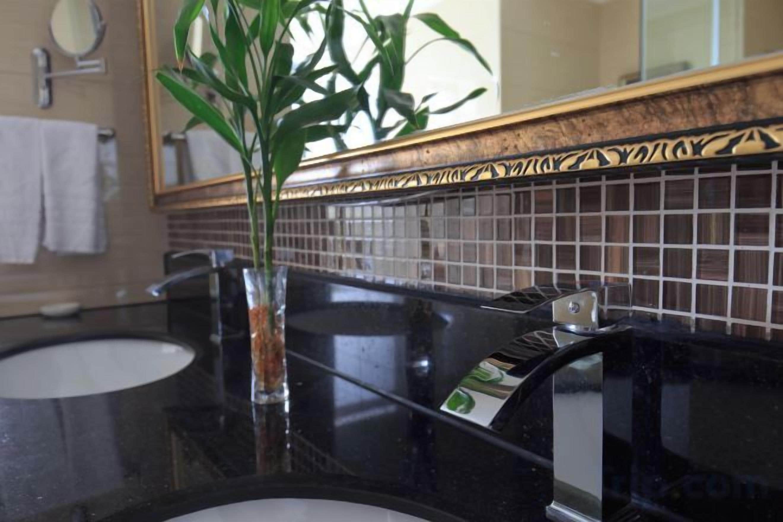 Une salle de bain avec deux lavabos, un miroir et une plante dans un vase en verre.