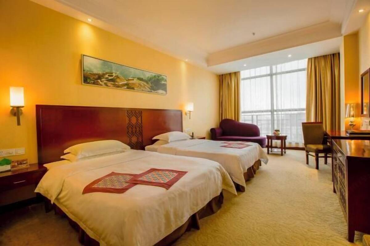 Une chambre d’hôtel avec deux lits, un bureau, une chaise et une grande fenêtre.
