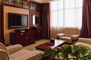 Una sala de estar con una televisión de pantalla plana, chimenea, sofá, mesa de centro y un ventanal con cortinas.