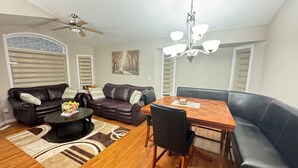 A living room with a brown leather sofa, a wooden coffee table, a dining table with chairs, and a chandelier. - 3 Bedrooms - Main Floor of House (Edmonton)