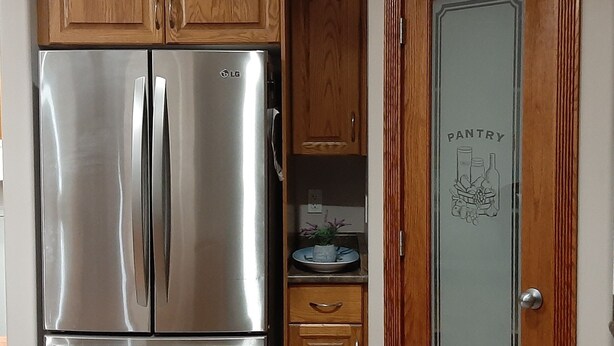 A stainless steel refrigerator in a kitchen with wooden cabinets and a pantry door. - 3 Bedrooms - Main Floor of House (Edmonton)