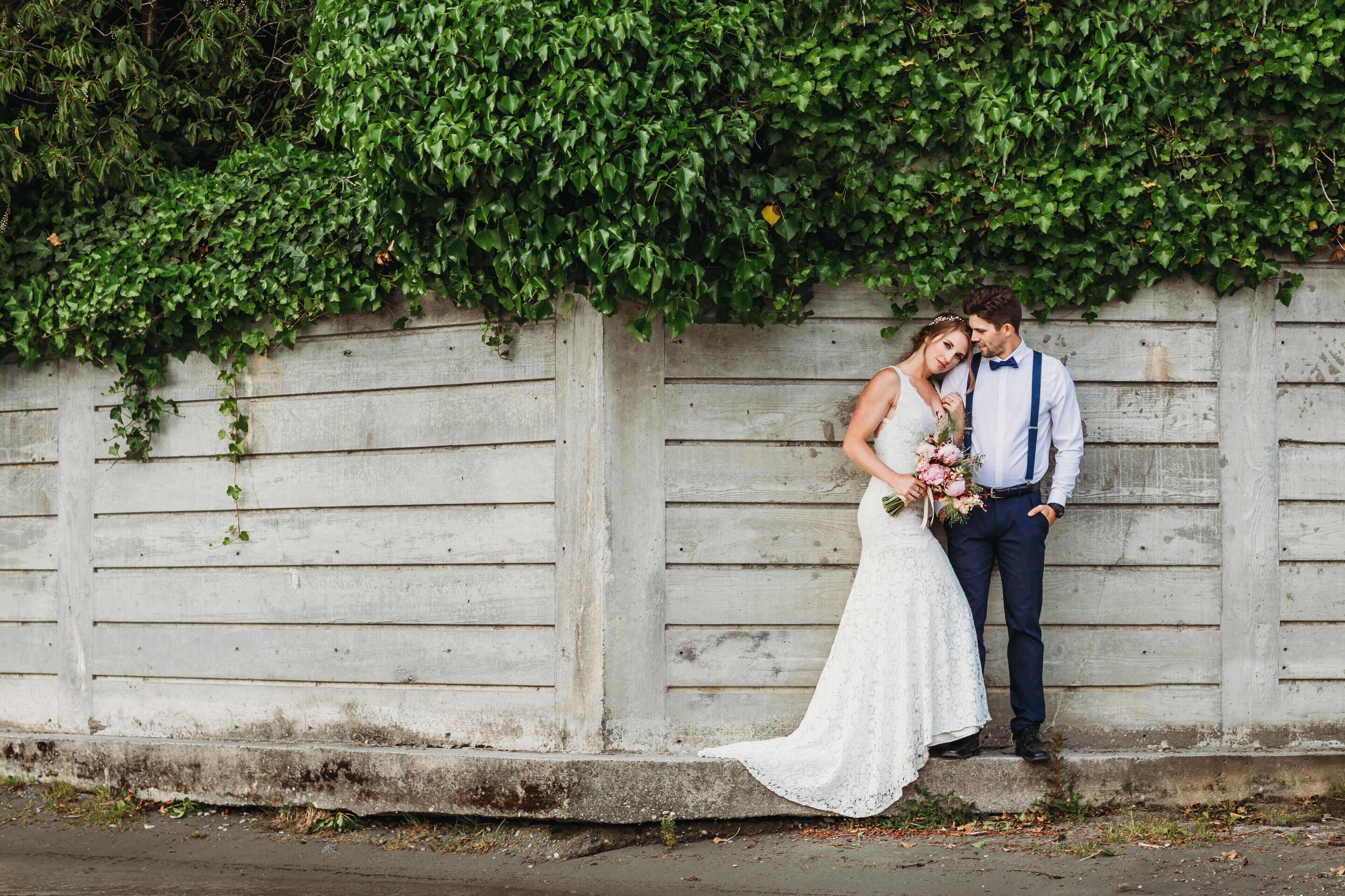 A couple standing against a wooden wall with greenery above.