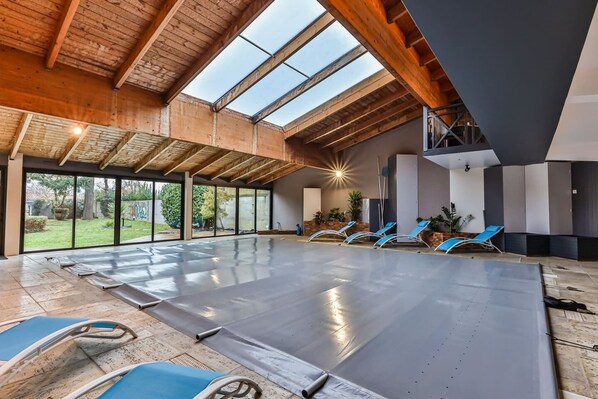 Un espacio interior amplio con techo alto, ventanas grandes y una zona de piscina con sillones de descanso.