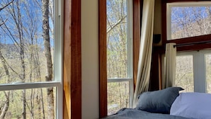 A bedroom with a large window offering a view of trees and a forest. - Eagle Ridge Treehouse (Stockbridge)