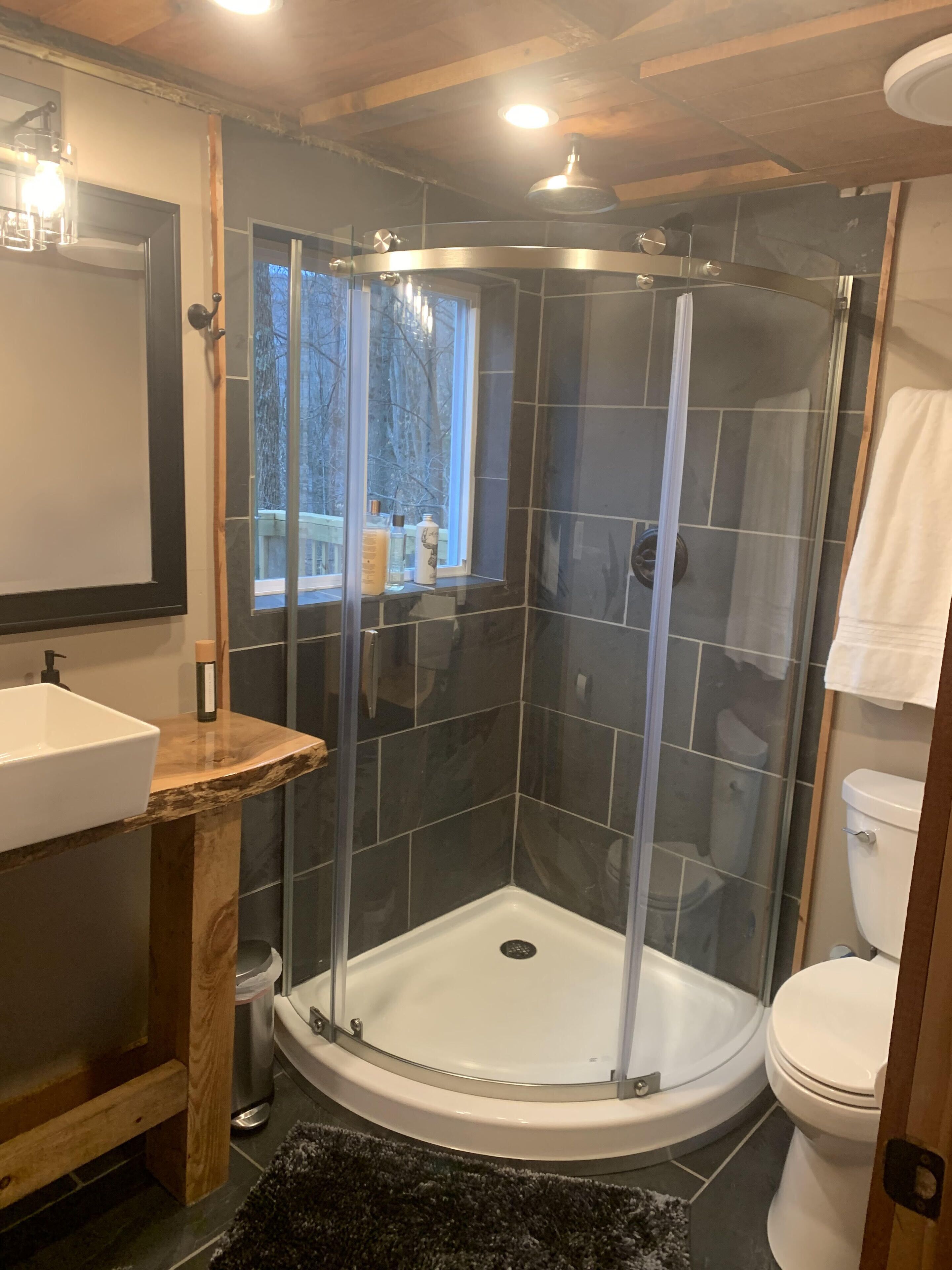 A modern bathroom with a glass-enclosed shower, a wooden vanity, and a white toilet.
