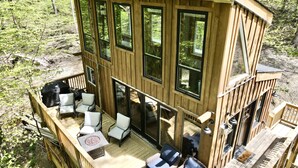 A wooden cabin with a deck, outdoor seating, and large windows. - Eagle Ridge Treehouse (Stockbridge)