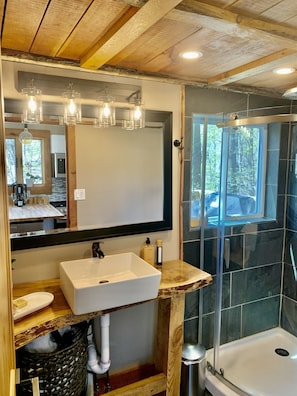 A bathroom with a large mirror, a sink, a shower, and wooden beams on the ceiling.