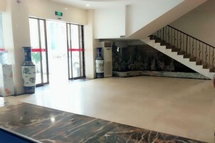 Un vestíbulo con mostrador de recepción de mármol, una escalera y grandes jarrones.