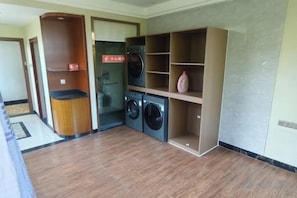 A laundry area with a washing machine and dryer, a small shelf, and a door leading to another room. - Bishui Lantian Hotel (Funing)